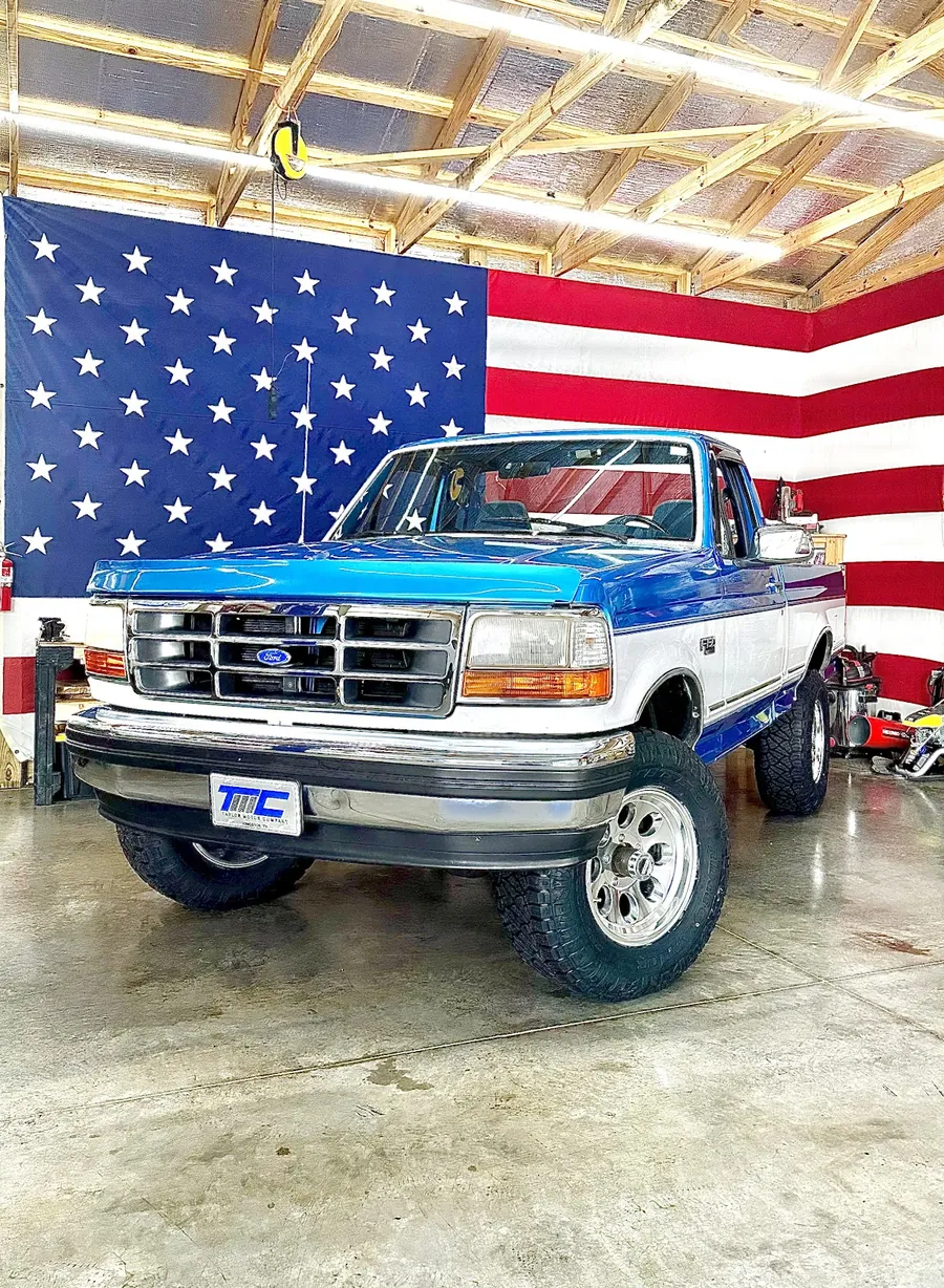 Two-tone Ford truck with a suspension lift in the MPG Automotive bay.